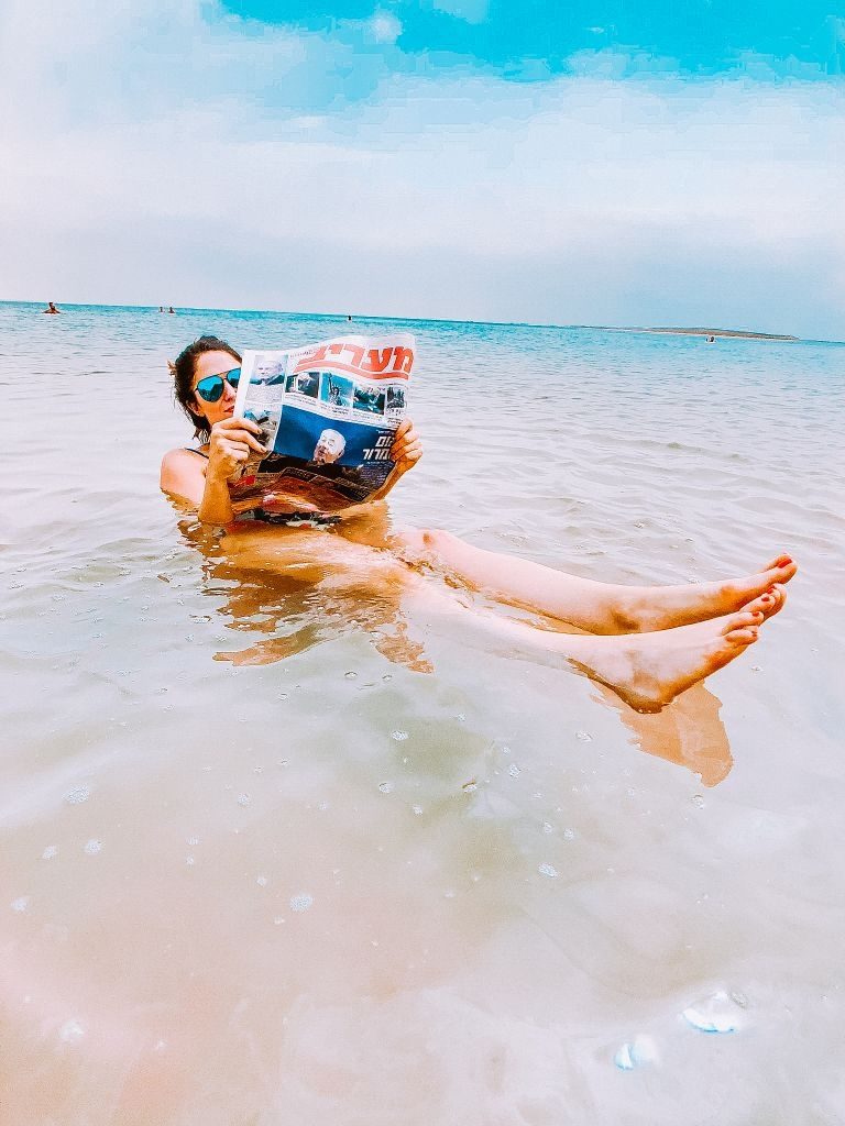 Girl floating in the Dead Sea reading a newspaper