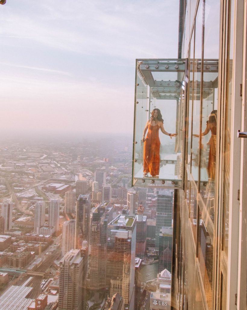 Girl statnding on the glass ledge over the city of Chicago