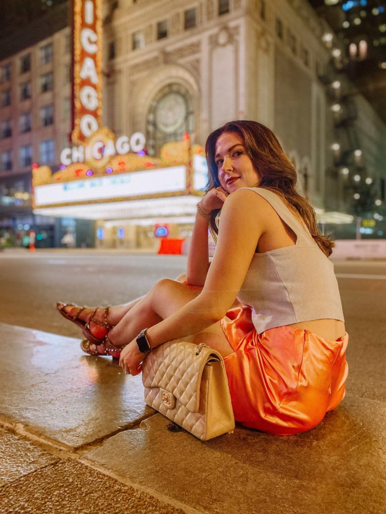 Girl sitting on the side walk in front of the Chicago Theater at night